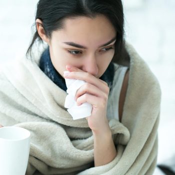 woman who has a cold with blanket wrapped around her and tissue in hand