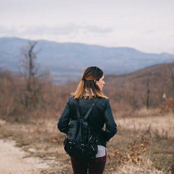 Girl with a black leather backpack exploring the nature.