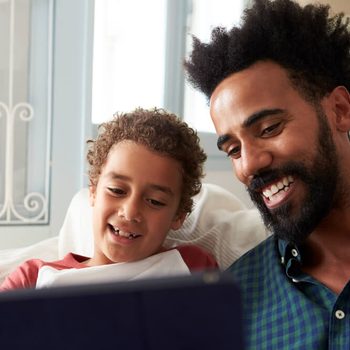 Father And Son Sitting On Sofa Using Digital Tablet