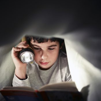 caucasian child reading book under the covers at night. Front view, copy space