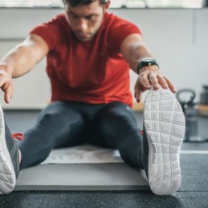 strong man stretching legs before gym workout. Fitness sporty male athlete on floor mat and towel warming up.