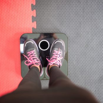 Woman standing on weigh scales at gym.Waist measurement by tape measure .Concept of healthy lifestyle.