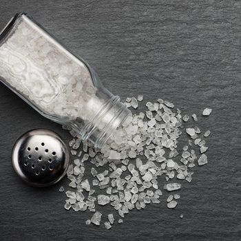 sprinkled salt shakers of white salt on the stone black background, top view