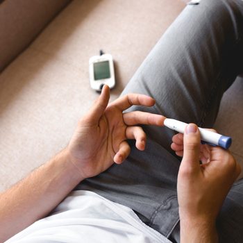 Handsome stylish young teen caucasian white brunette guy man european taking a blood sample with a glucometer to measure sugar level,lancet on finger diabetes, glycemia meter top first view shot