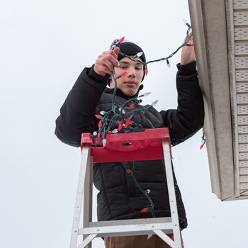 Man hanging Christmas lights during winter from a ladder