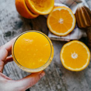 Woman Hand with juice glass and Oranges on wooden background.