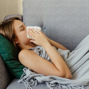 The sick woman, holding a handkerchief, sneezing and feeling freezing, lying on the bed, at home. Health problem.