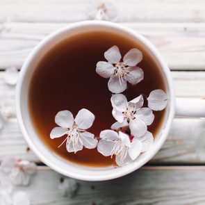 Cup of tea and spring apricot blossom on a white wooden background. Overhead view. Rustic.