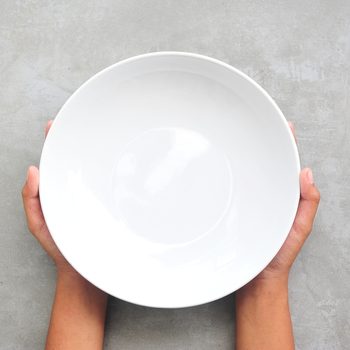 Female hands hold empty dish on stone background.