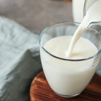 Pouring of milk into glass on table