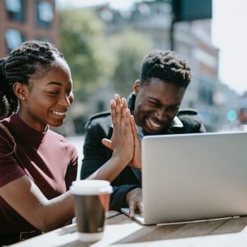 two students high-fiving behind open laptop