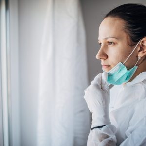 worried doctor looking out the window with gloves and mask on