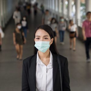 Asian woman with protective face mask in the urban bridge in city against crowd of people