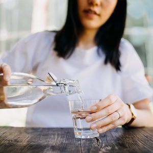 Woman pouring water from bottle into the glass at a outdoor cafe