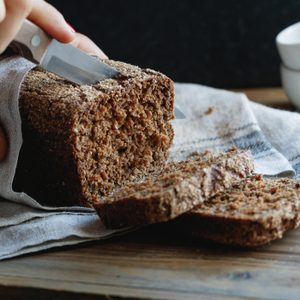 The girl cuts whole-wheat rye bread on a wooden table.