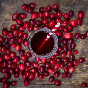 Cranberries surrounding glass of cranberry juice