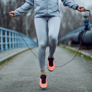 Unrecognizable sportswoman jumping rope on a bridge.