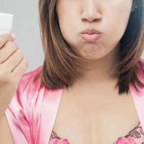 Midsection Of Young Woman Gargling Against Gray Background