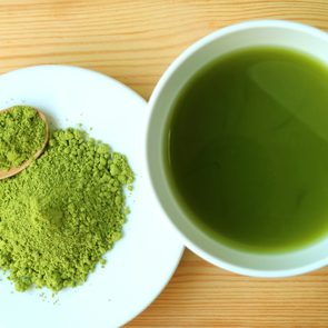 Top View of a Cup of Hot Matcha Green Tea with a Plate of Matcha Tea Powder on Wooden Table