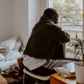 Rear view man looking through window while sitting in bedroom