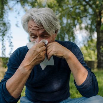 man blowing nose while sitting in field