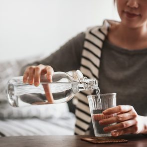 close up of young woman pouring herself a glass of water at home