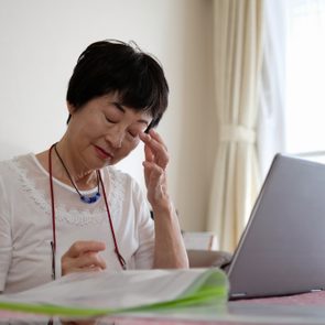 Senior woman rubbing eye while working at home