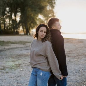 Man and woman standing back to back on the beach