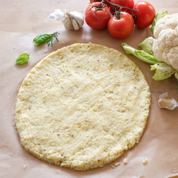 raw pizza base from shredded cauliflower on baking paper, healthy vegetable alternative for low carb and ketogenic diet, copy space