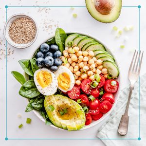 top view of a bowl filled with blueberries, avocado, hard boiled eggs, tomatoes and chick peas