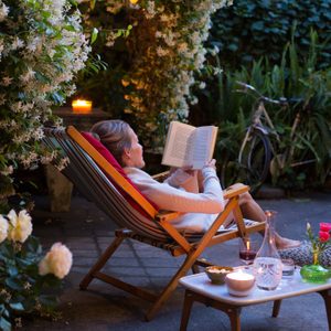 Woman relaxing on deck chair in back yard, reading a book with her cat watching