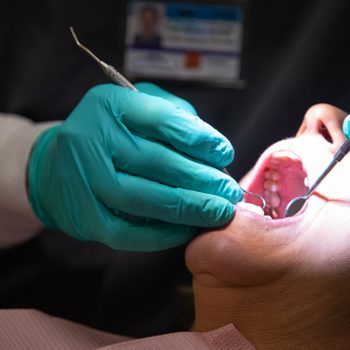 A Dentist Wearing Surgical Gloves Uses A Loupe Light To Examine The Teeth Of A Female Patient In Her Sixties In A Dental Clinic